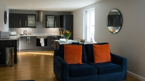 Een moderne keuken met donkere kastjes, een zithoek met een blauwe bank, en een grote spiegel aan de muur.