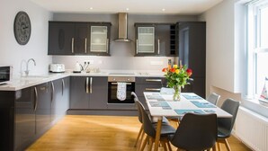 Een moderne keuken met donkere kastjes, een centraal eiland en een eethoek met een tafel en stoelen.