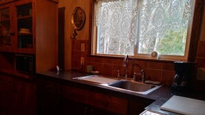A kitchen with a sink, stove, and window with lace curtains. - Cozy one bedroom tiny house. (Colville)