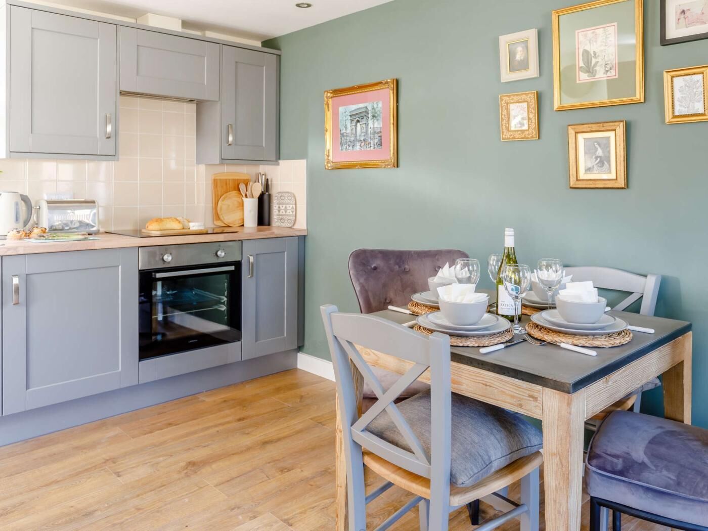 Une cuisine avec des meubles de couleur grise, un plan de travail en bois et un coin repas avec une table dressée pour deux personnes.