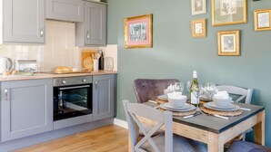 Une cuisine avec des meubles de couleur grise, un plan de travail en bois et un coin repas avec une table dressée pour deux personnes.