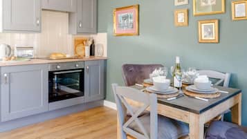 Une cuisine avec des meubles de couleur grise, un plan de travail en bois et un coin repas avec une table dressée pour deux personnes.