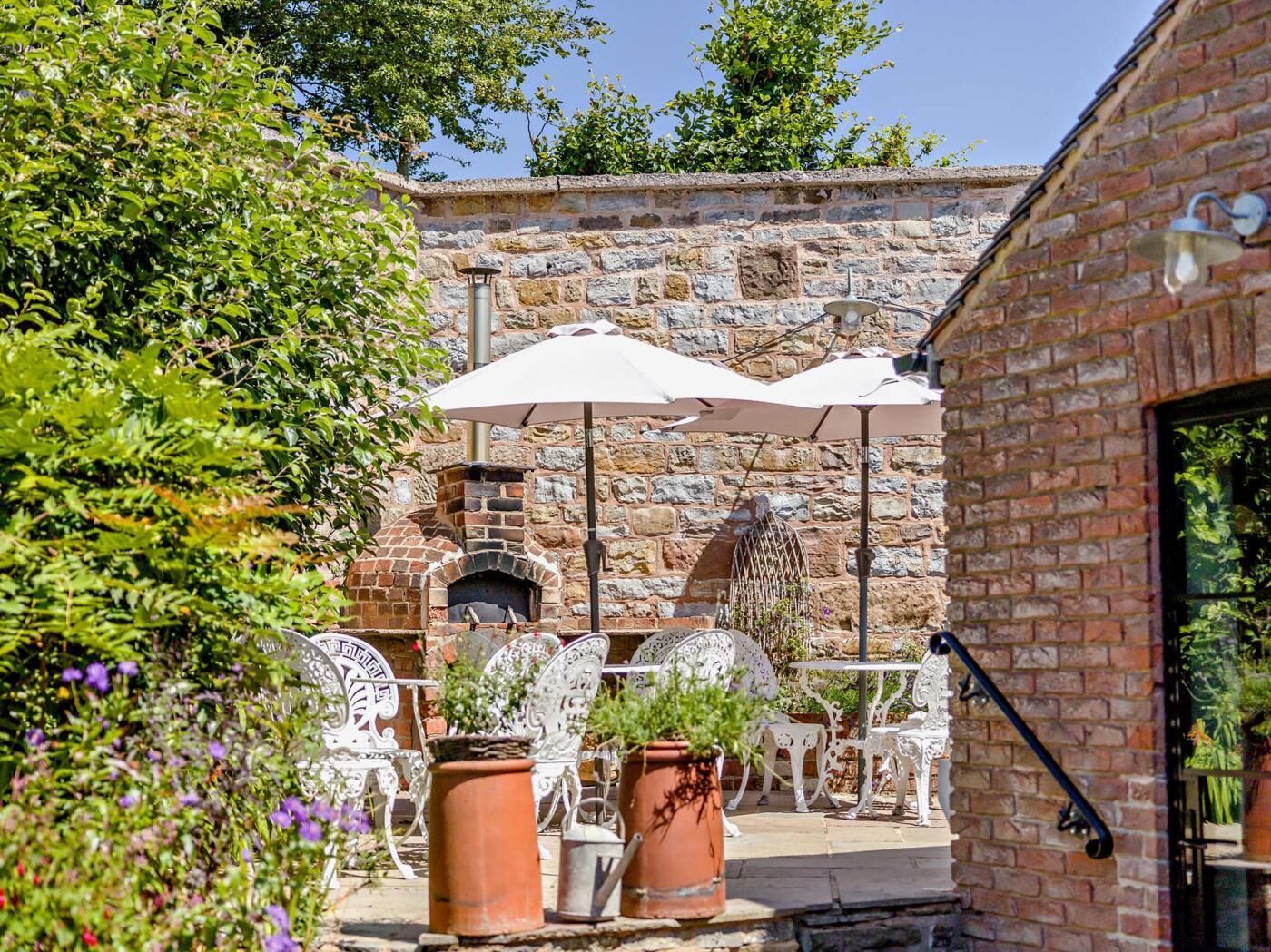 A stone building with a brick fireplace, outdoor seating with white chairs and tables, and potted plants.