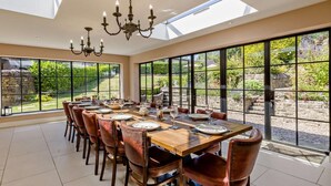 A dining area with a long table, chairs, and a chandelier. - 7 Bed in Stoke-on-trent (oc-81529) (Waterhouses)
