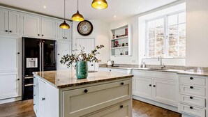 Een moderne keuken met witte kasten, een centraal eiland, hanglampen, een klok en een raam met uitzicht.