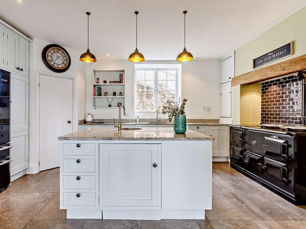 A modern kitchen with white cabinetry, a central island, pendant lighting, a brick backsplash, and a clock on the wall.