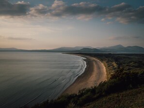 A coastal landscape with a beach, distant mountains, and a clear sky. - 4 Bed in Blaenau Ffestiniog (oc-81060) (Gellilydan)