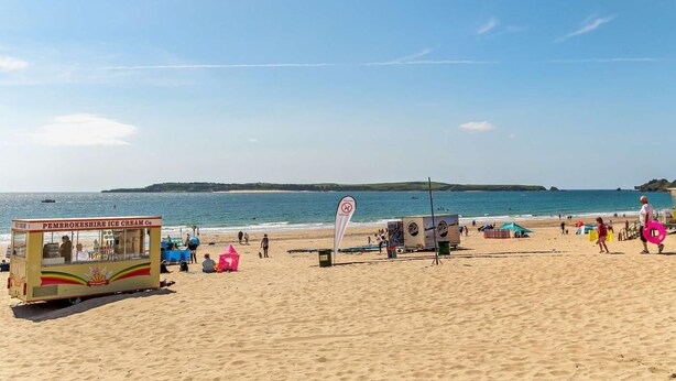 A beach with a food truck, beachgoers, and a clear sky. - 2 Bed in Tenby (oc-fb261) (Tenby)