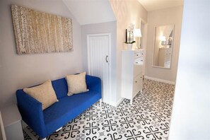 Ein Flur mit einem blauen Sofa, einem weißen Schrank, einem Spiegel und Fliesen mit Muster.
