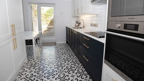 A modern kitchen with white cabinets, a black and white patterned floor, and a built-in oven. - 2 Bed in Tenby (oc-fb261) (Tenby)