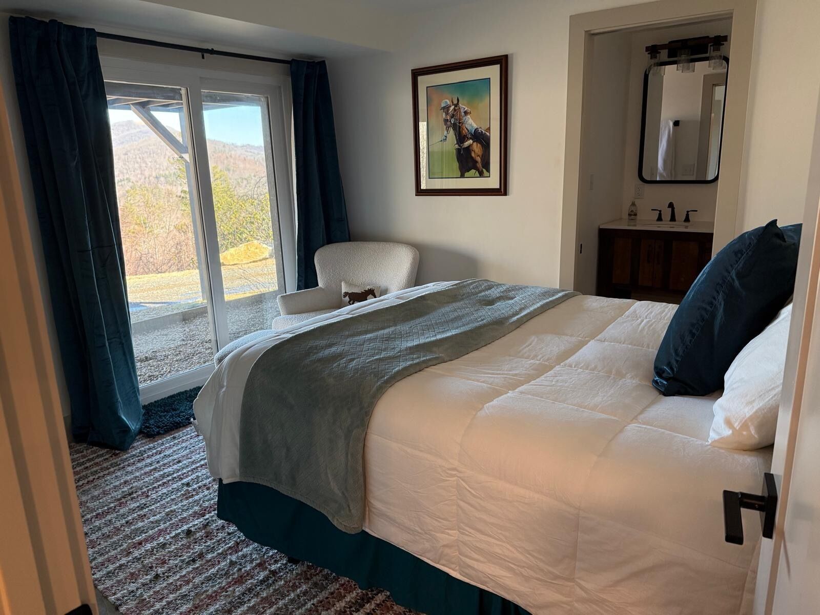 A hotel room with a bed, a chair, a painting, and a window with curtains.