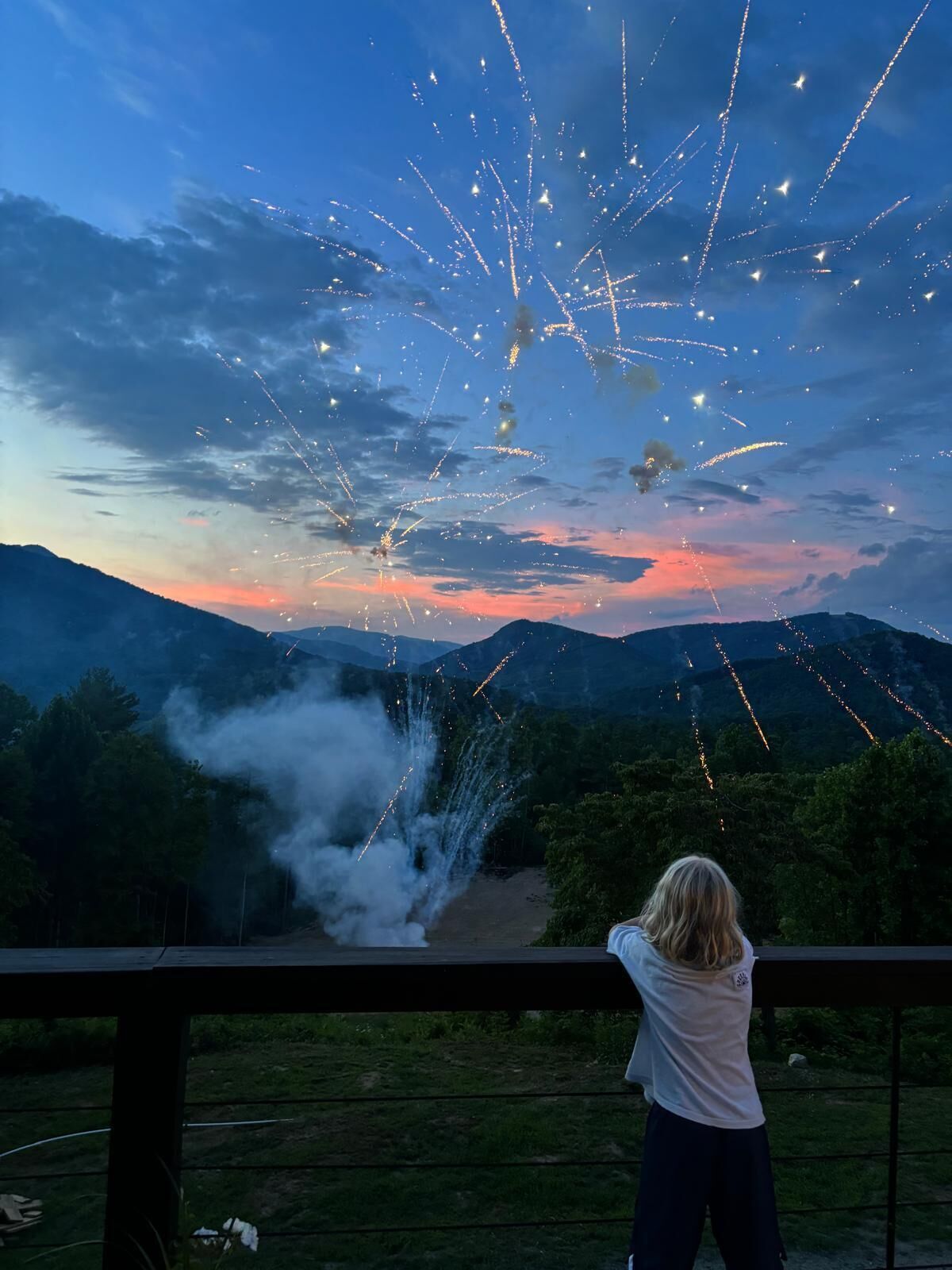 A person overlooking a fireworks display with mountains in the background.