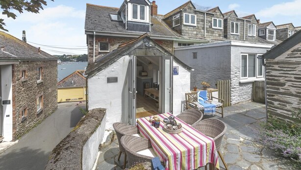 Un bâtiment en pierre doté d’un petit patio, d’une table avec des chaises et d’une vue sur la mer.