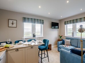 A modern kitchen with a dining area, a blue sofa, and a TV mounted on the wall.