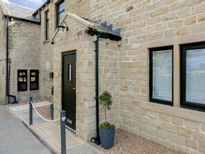 A stone building with a black door, windows, and a small garden area with a potted plant.