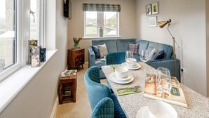 Ein modernes Wohnzimmer mit einem blauen Sofa, einem Esstisch mit Tellern und Gläsern sowie einem Fenster mit Vorhängen.