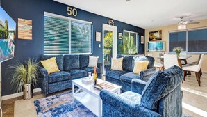 Ein modernes Wohnzimmer mit einem blauen Sofagarnitur, einem weißen Couchtisch und einem Essbereich mit Tisch und Stühlen.