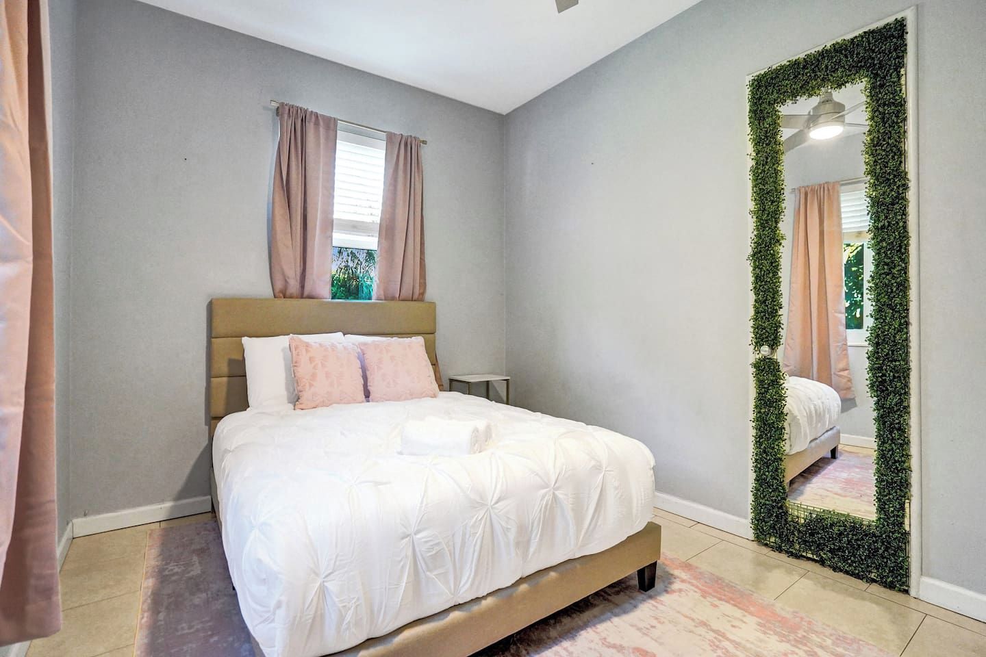 A bedroom with a bed, curtains, a mirror, and a green plant wall.