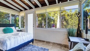 Ein Schlafzimmer mit einem Bett, einem Schreibtisch und einem Fenster mit Blick auf Bäume.
