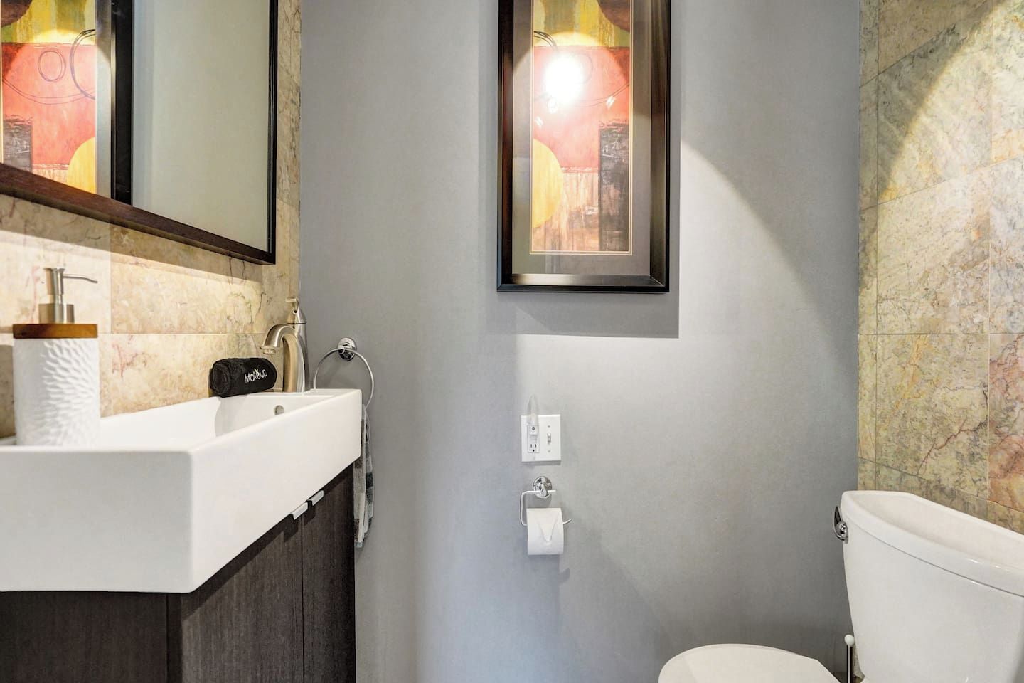 Ein Badezimmer mit einem weißen Waschbecken, einem Spiegel, einer Toilette und einem gerahmten Bild an der Wand.
