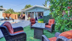 Ein Garten mit Schwimmbad, Korbmöbeln und einer überdachten Terrasse.