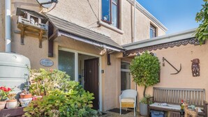 Una casa con un giardino, un patio con tavolo e sedie e un piccolo albero.