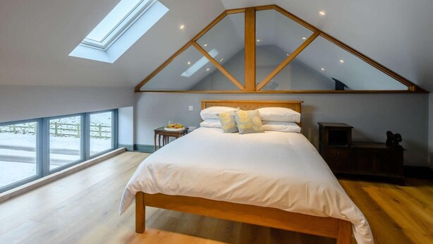 Un dormitorio con techo inclinado, tragaluz, estructura de cama de madera y vista al exterior.