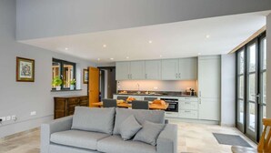 Un amplio espacio habitable con un sofá gris, una mesa de comedor y una cocina al fondo.