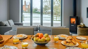 Una sala de estar moderna con un ventanal grande, una chimenea y una mesa de comedor dispuesta para el desayuno.