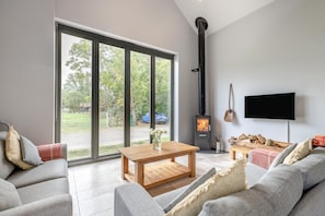 A modern living room with a fireplace, large windows, and a flat-screen TV. - 1 Bed in Little Gransden (oc-81056) (Little Gransden)