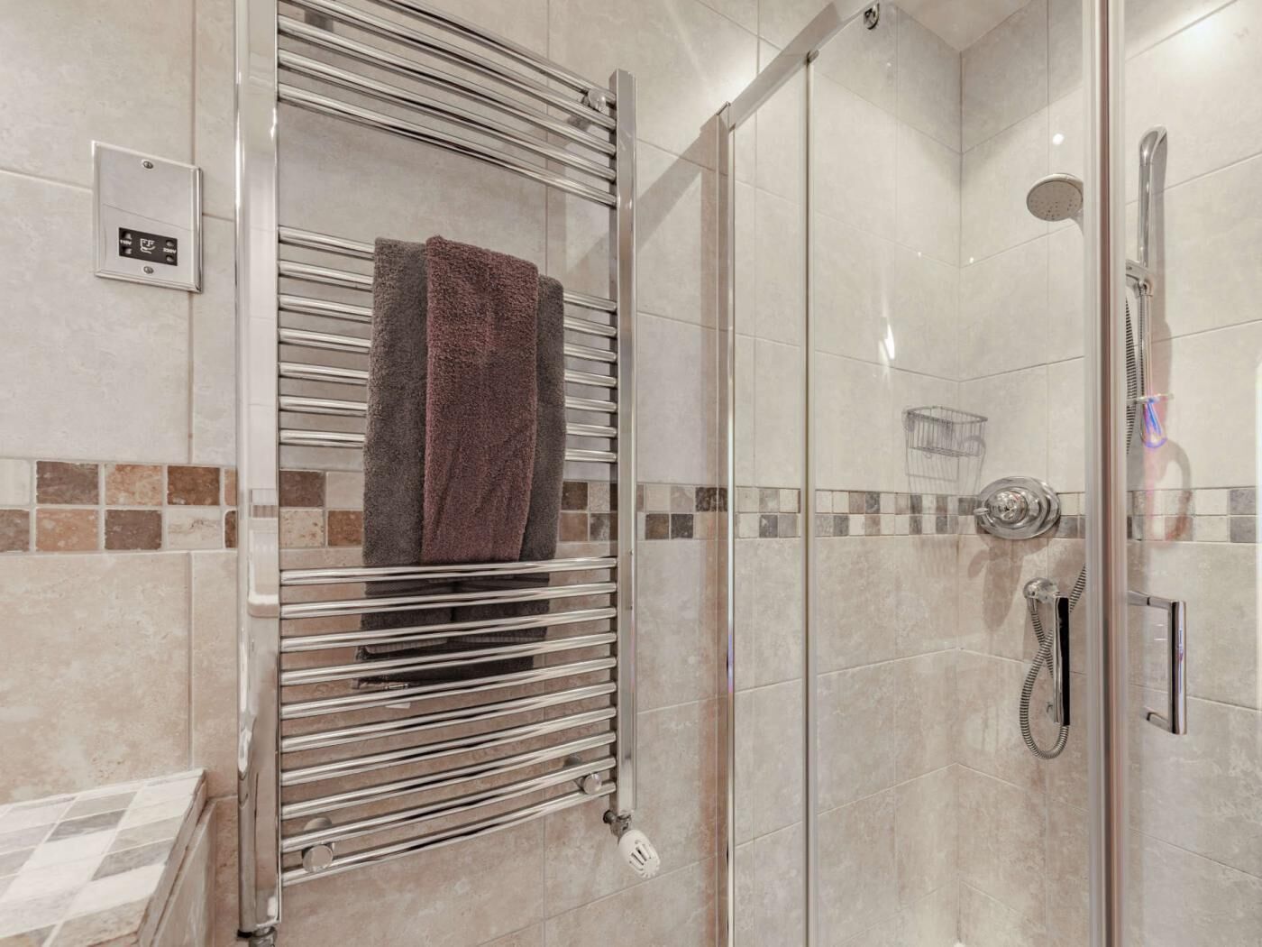 Een moderne badkamer met een douchecabine van glas, een handdoekhouder met een handdoek, en een bedieningspaneel aan de muur.