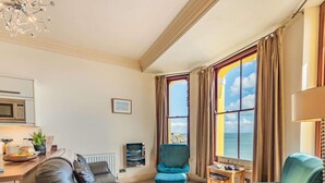 A living room with a sofa, two armchairs, a coffee table, a TV, and a view of the sea. - 2 Bed in Tenby (oc-fb233) (Tenby)