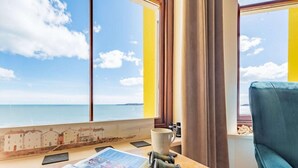 A room with a large window overlooking a body of water, a table with a magazine, a cup, and salt shakers. - 2 Bed in Tenby (oc-fb233) (Tenby)