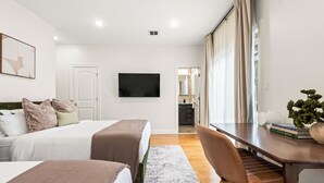 Ein modernes Hotelzimmer mit Bett, Schreibtisch, Stuhl, Fernseher und Blick auf die Küche.