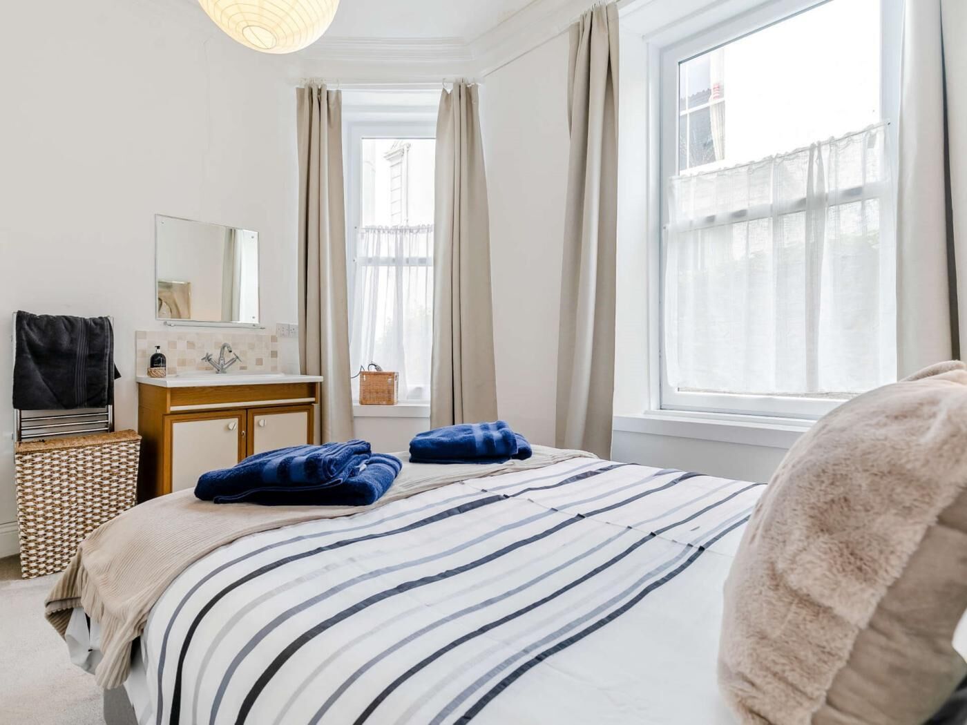 Un dormitorio con cama, mesita de noche, espejo, ventana con cortinas y vistas al exterior.