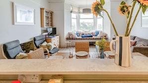 A living room with a sofa, a dining table set, a television, and a bookshelf. - 3 Bed in Fowey (oc-81112) (Fowey)