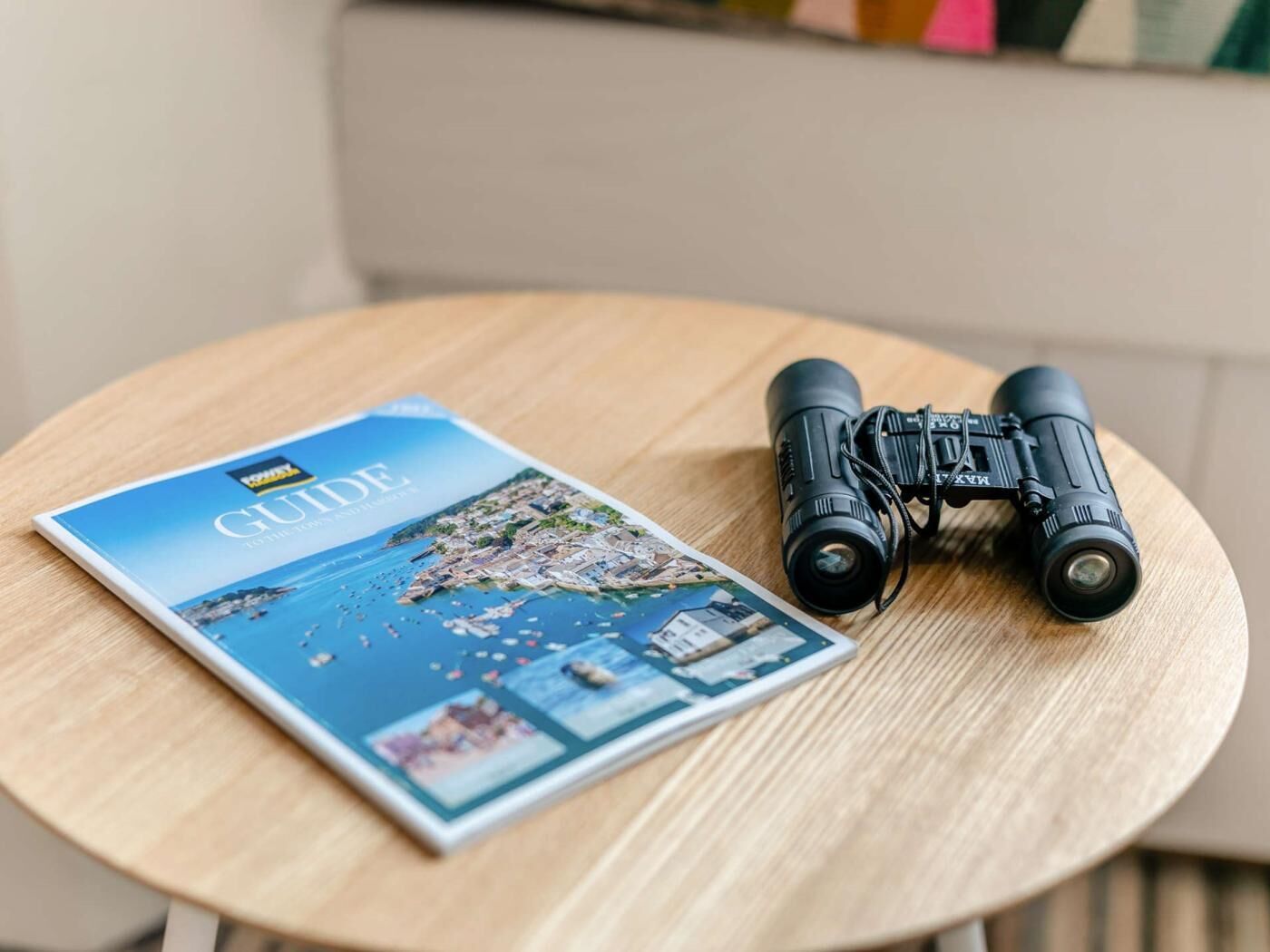 A guidebook and binoculars on a round wooden table.