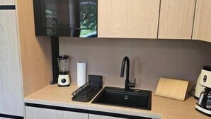Et kompakt køkken med en sort vask, en blender og en kaffemaskine.