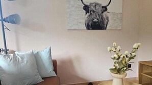 En stue med en brun sofa, en hvid vase med blomster, en lampe og et billede i ramme på væggen.