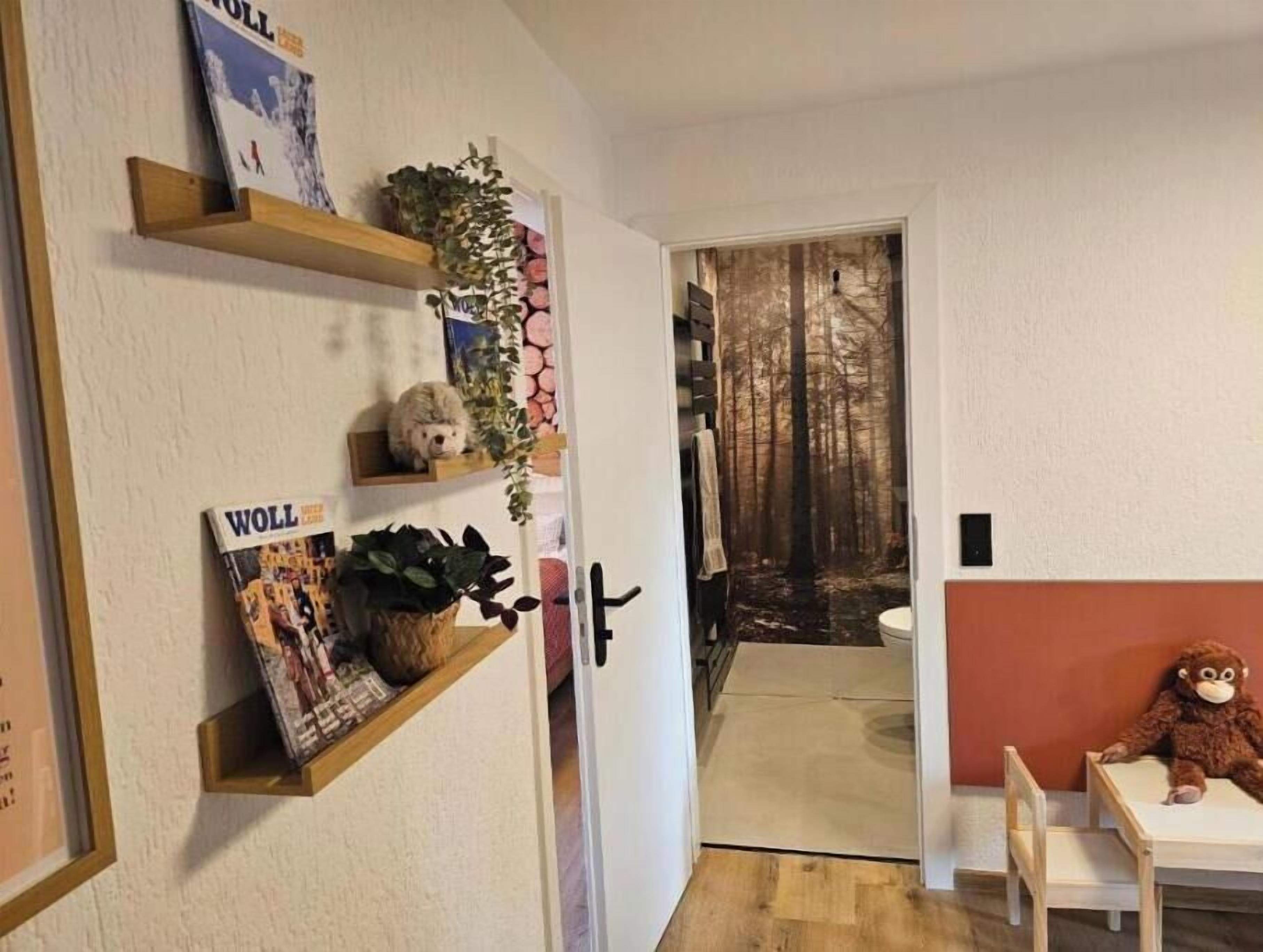 A hallway with wooden shelves, a plush toy, and a door leading to a room with a view of trees.