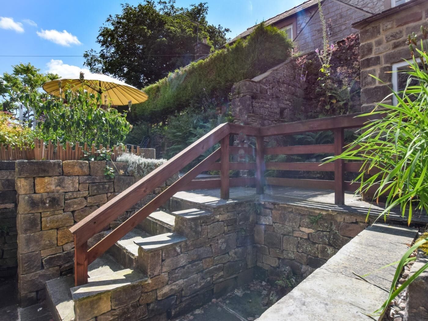A stone staircase with a wooden handrail leading to a stone wall.