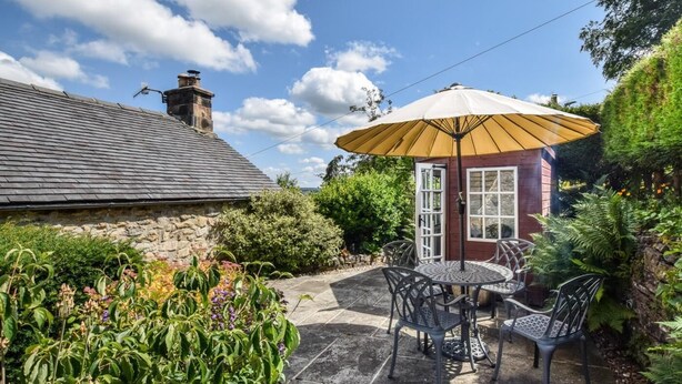 Ein Steinhaus mit einer gefliesten Terrasse, einem runden Tisch mit Stühlen und einem großen Sonnenschirm.