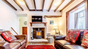 Ein gemütliches Wohnzimmer mit Ledersofas, einem roten Teppich mit Muster, einem Kamin aus Stein und einem Fernseher darüber.