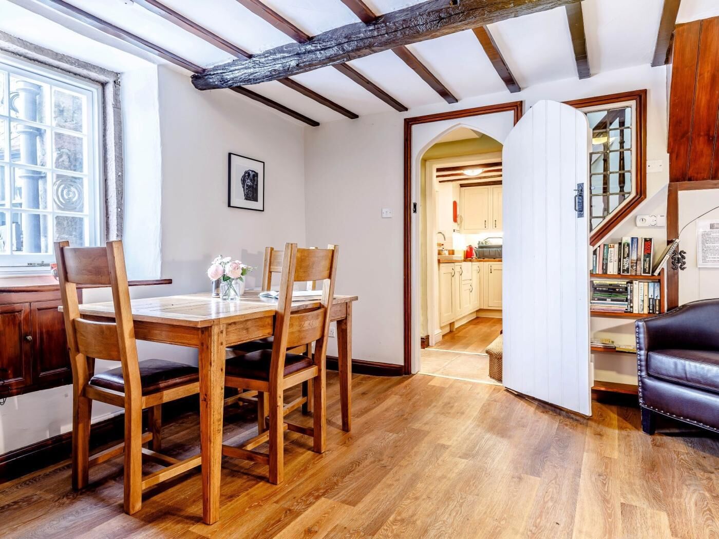 Un comedor con muebles de madera, una ventana con vistas y una cocina visible a través de un vano abierto.