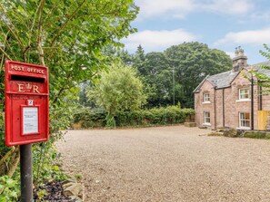 A red post office sign with a mailbox, a gravel driveway, and a stone building in the background. - 4 Bed in Matlock (oc-82198) (Cromford)