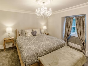 Ein Schlafzimmer mit einem großen Bett, zwei Nachttischen, einer Kronleuchter und einem Fenster mit Vorhängen.
