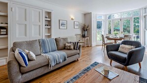 Un salon comprenant un canapé, un fauteuil, une table basse et un coin repas, le tout baigné de lumière naturelle.