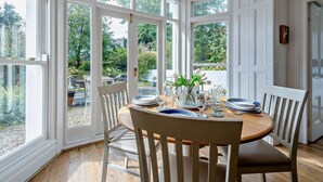 Un coin repas avec une table ronde, des chaises et une vue sur le jardin grâce à de grandes fenêtres.
