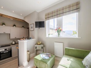 A modern kitchen with built-in appliances, a dining area with a green sofa, and a window with a view. - 1 Bed in Holmfirth (oc-82194) (Meltham)