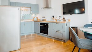 A modern kitchen with light blue cabinets, a stainless steel range hood, a built-in oven, and a flat-screen TV mounted on the wall. - 2 Bed in Tenby (oc-fb285) (Tenby)